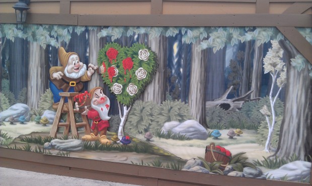 Dwarfs painting the roses red, on the construction wall across from Mad Tea Party