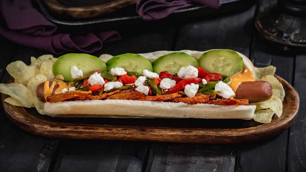 At Refreshment Corner at Disneyland Park, guests will find this Hades-inspired foot-long all-beef hot dog served with harissa aioli, lemon pickled cucumbers, oven dried tomatoes, sautéed peppers and feta cheese. (David Nguyen/Disneyland Resort)