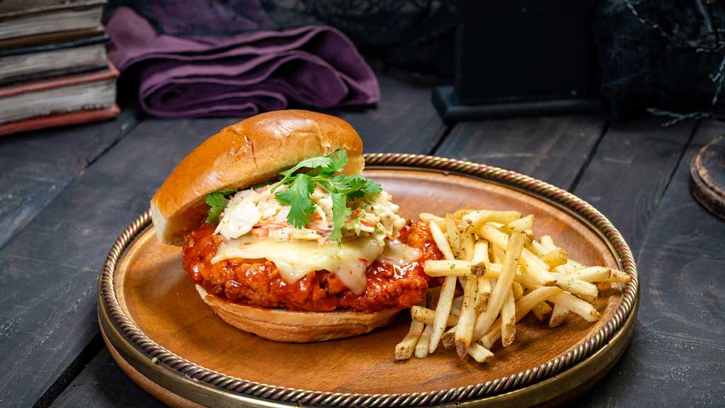 At Carnation Café at Disneyland Park, guests will find this Spicy Fried Chicken Sandwich featuring Sriracha-glazed fried chicken breast on a brioche bun with spicy sandwich spread, pepper Jack cheese, creamy mustard slaw, and cilantro served with fries. (David Nguyen/Disneyland Resort)