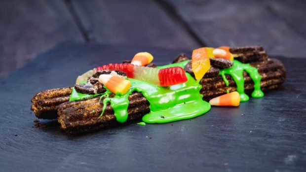 Disney guests will discover a variety of delicious treats during Halloween Time at Disneyland Resort, from Sept. 6 through Oct. 31, 2019. At Cozy Cone at Disney California Adventure Park, guests will find this specialty churro rolled in crumbled chocolate crème cookies, green icing, gummy worms and candies. (David Nguyen/Disneyland Resort)