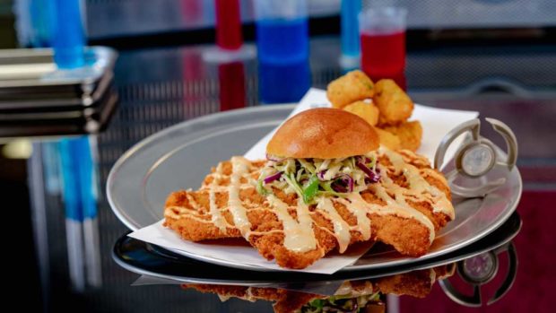 Experiment No. EE90: Not So Little Chicken Sandwich features fried chicken breast with teriyaki and red chili sauces, pickled cabbage slaw and crispy potato tots. (David Nguyen/Disneyland Resort)