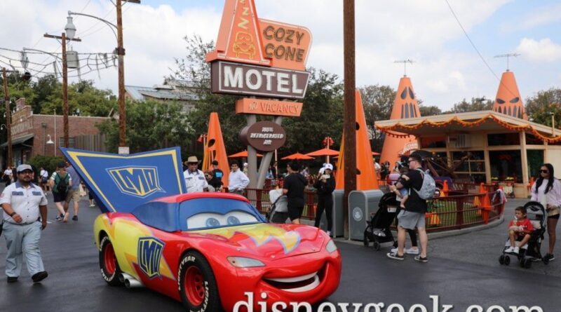 Lightning McQueen and the other residents of Radiator Springs are celebrating Haul-O-Ween. He is dressed as a super hero for Trunk or Treating. Here he is rolling along Route 66 by the Cozy Cone in Cars Land.